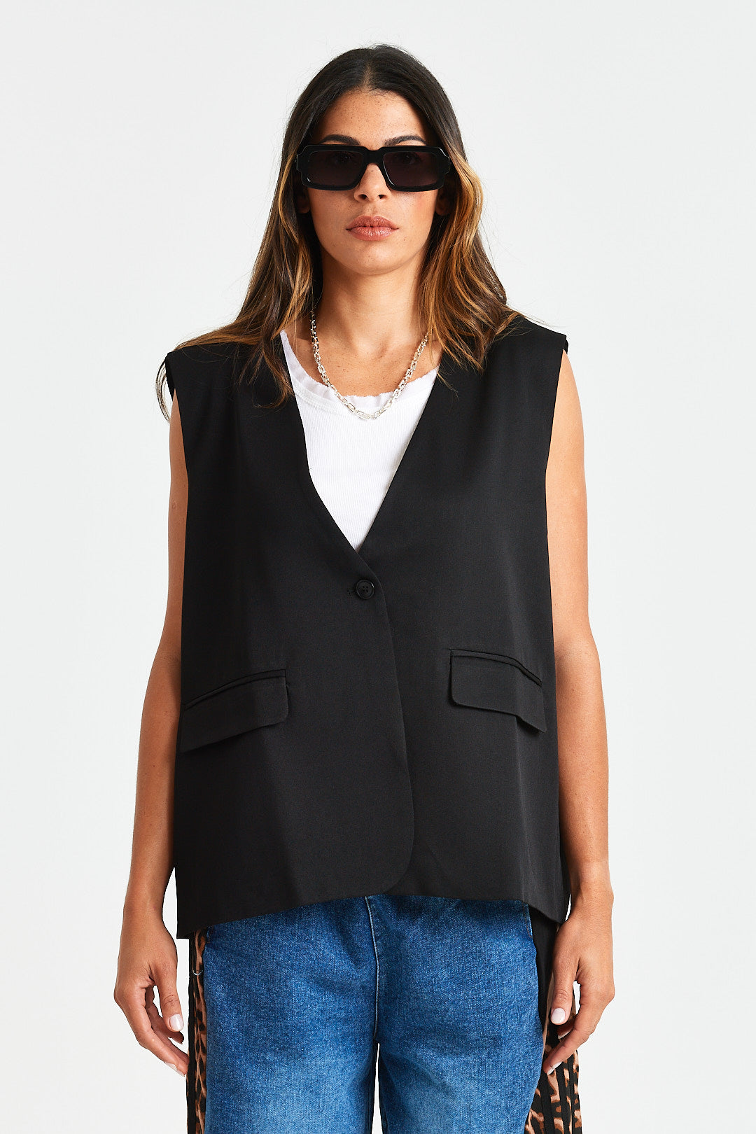 GABE WAISTCOAT Woman wearing a black vest over a white top and blue jeans on a white background