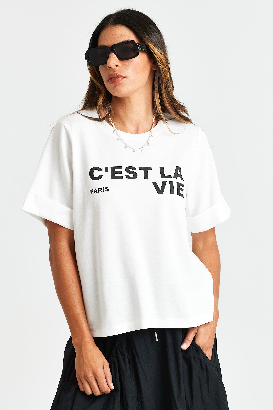 FRIDA TEE Woman wearing a white t-shirt with 'C'EST LA VIE PARIS' text on a plain background