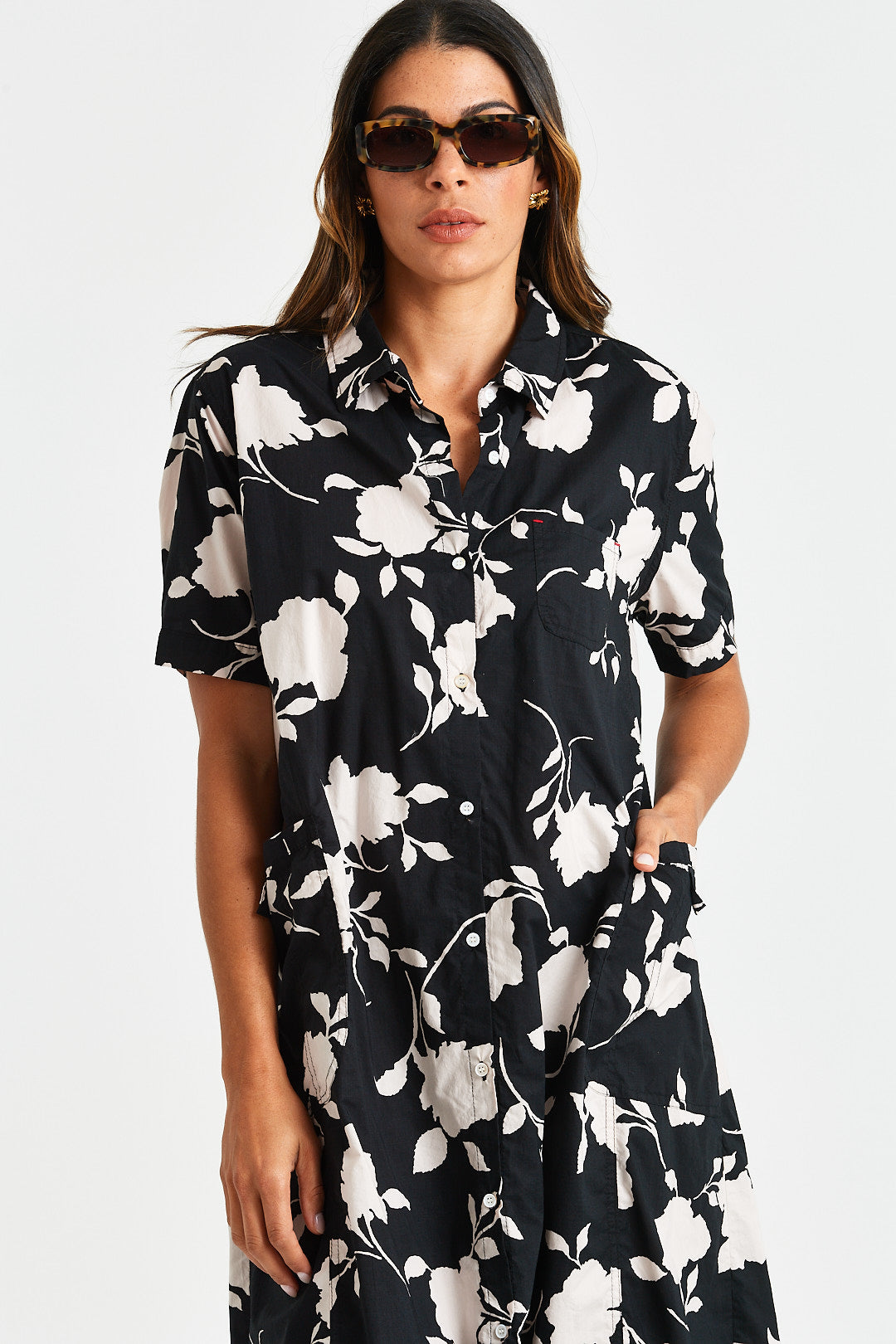 NOE DRESS Woman wearing a black floral dress with white flowers on a plain background