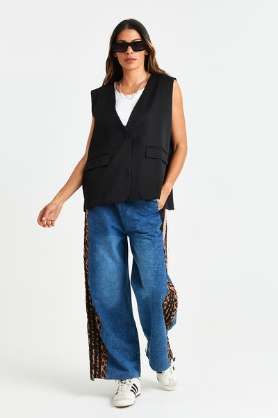 GABE WAISTCOAT Woman wearing a black vest, white shirt, blue jeans with animal print accents, and white sneakers on a white background.